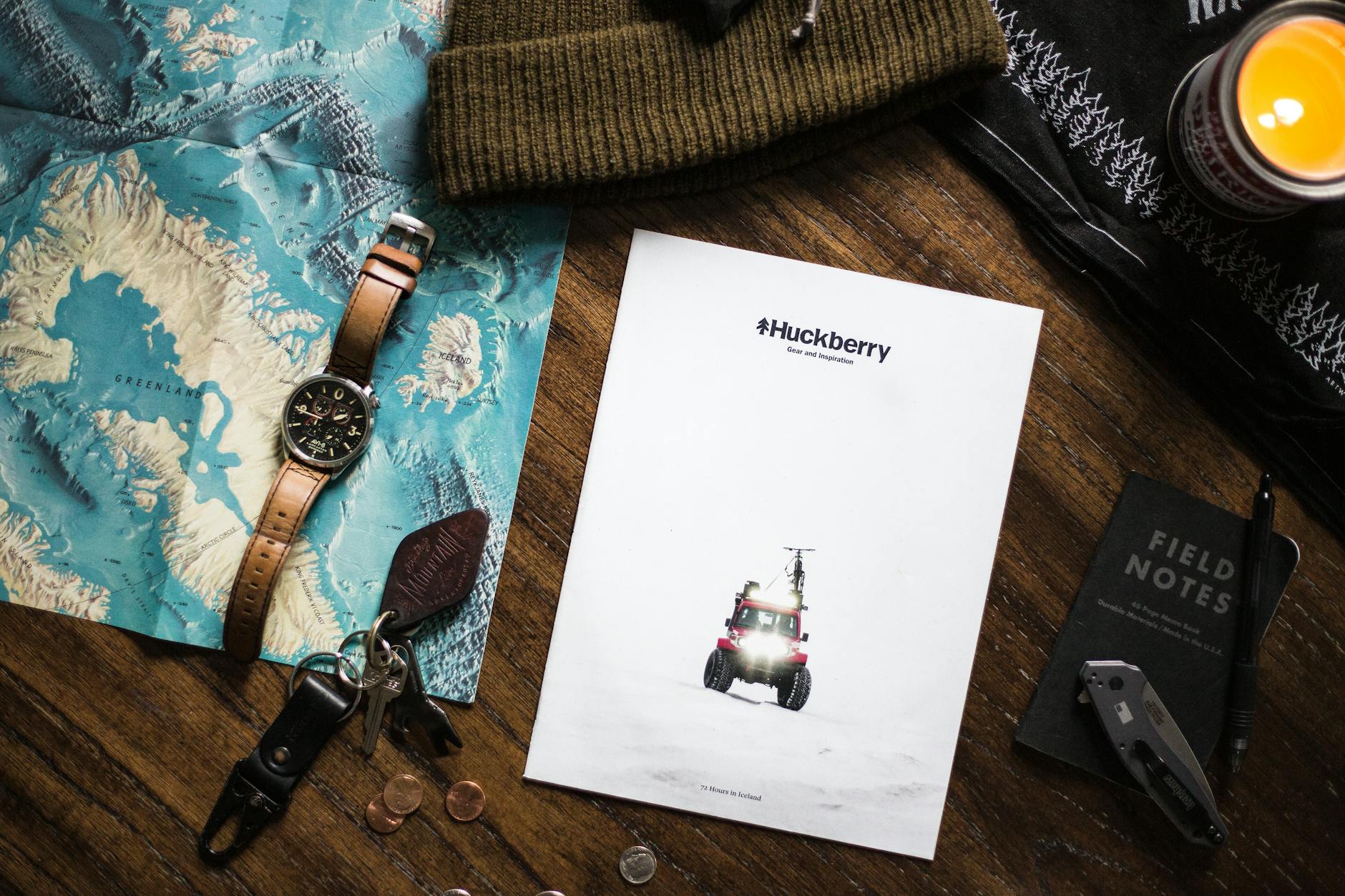 Flat lay of adventure essentials with map, watch, and Huckberry magazine, perfect for travel enthusiasts.