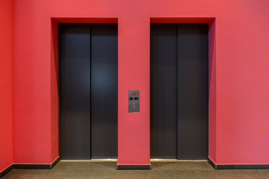 A pair of sleek modern elevator doors set against a vibrant red wall. Ideal for architectural themes.
