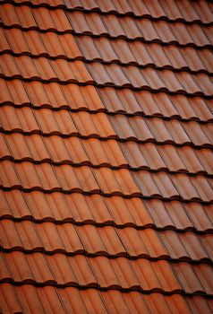 Detailed view of red clay roof tiles forming a repetitive pattern in warm sunlight.