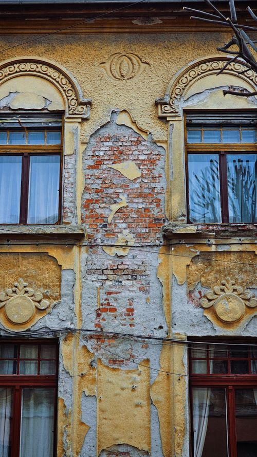 Free Close-up of an old building facade with ornate designs and peeling plaster, showing exposed red bricks. Stock Photo
