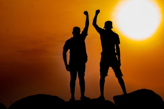 Two silhouetted figures raising fists triumphantly against a vibrant sunset in Ghana.