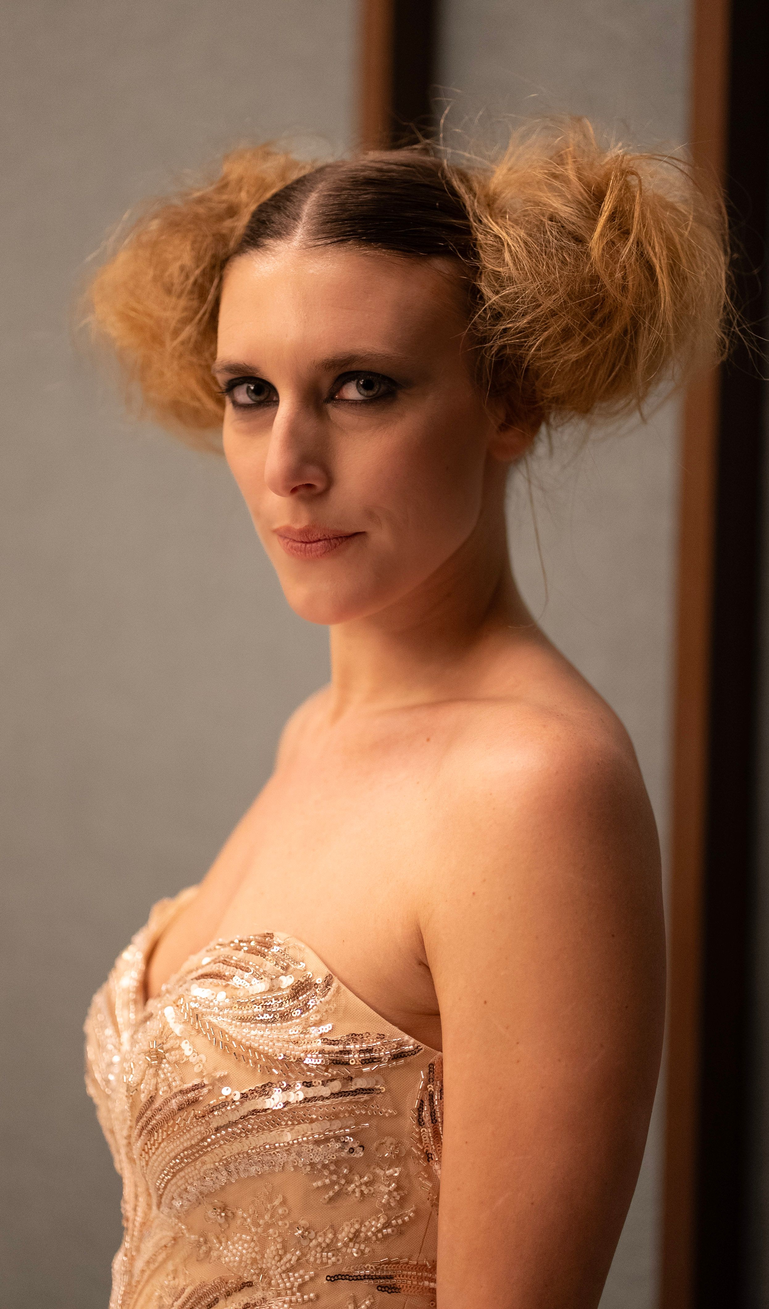 Fashion portrait of a model with a unique hairstyle wearing a designer dress, captured in a studio setting.