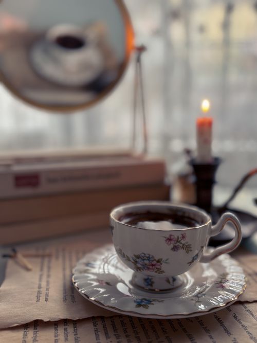 Free A vintage teacup with floral patterns in a warm ambient setting, reflecting in a round mirror. Stock Photo