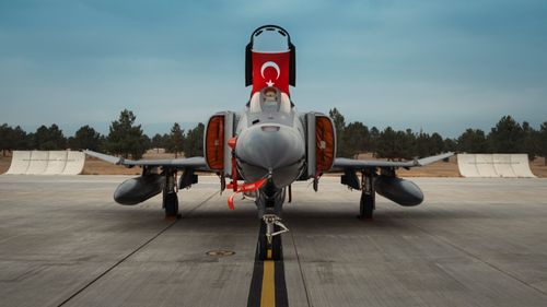 Free Front view of a Turkish military jet fighter showcasing its national flag on a runway. Stock Photo