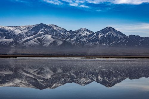 Free Beautiful snow-capped mountains reflected perfectly in a calm body of water under a clear blue sky. Stock Photo