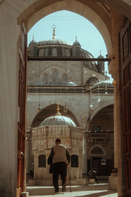 Free Man entering a mosque in Istanbul, showcasing detailed architecture and ambient lighting. Stock Photo