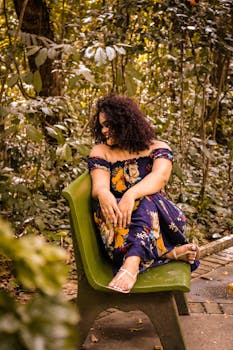 Young woman with curly hair enjoys a sunny day sitting on a bench in a lush Brazilian park.