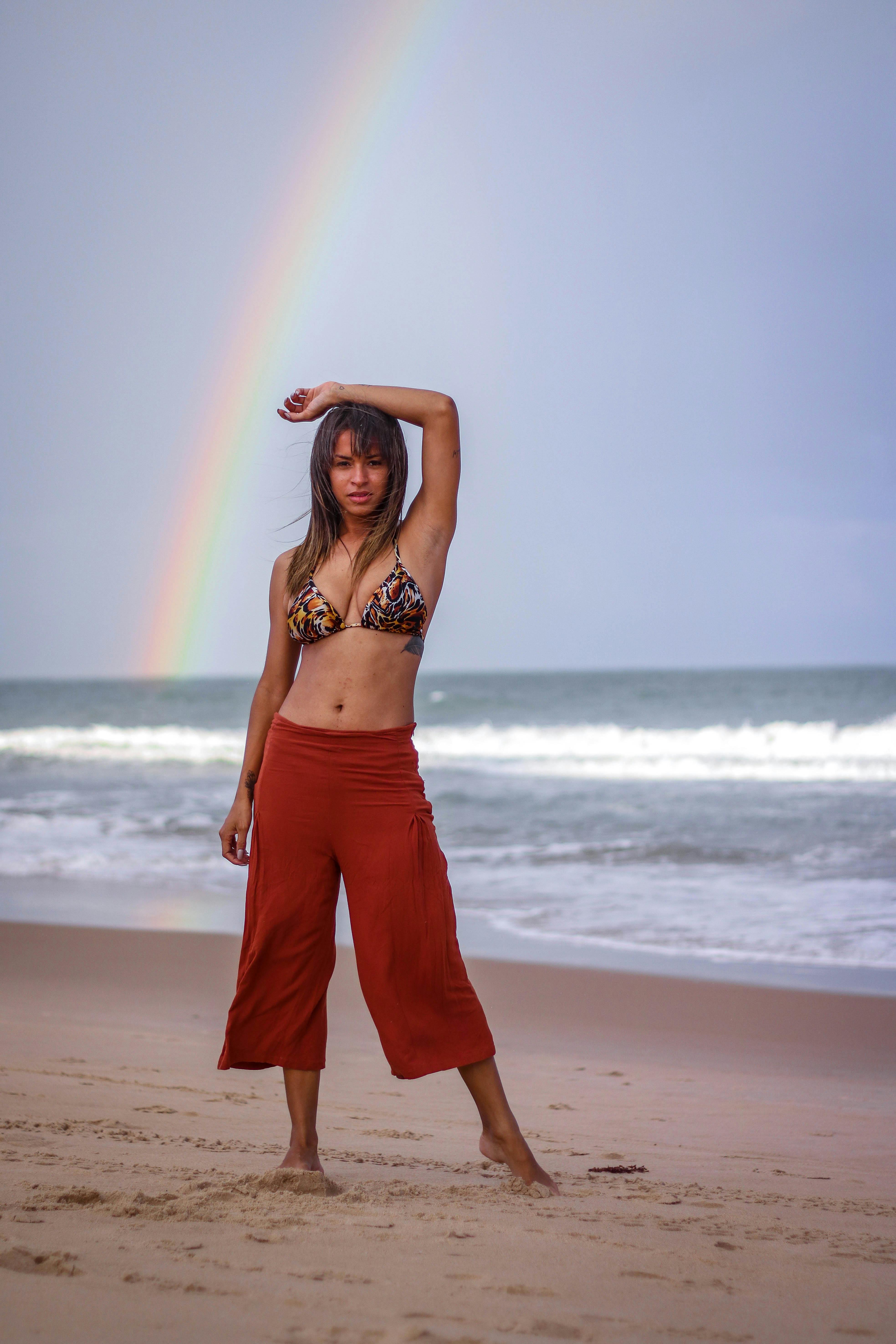 woman standing on seashore overlooking rainbow