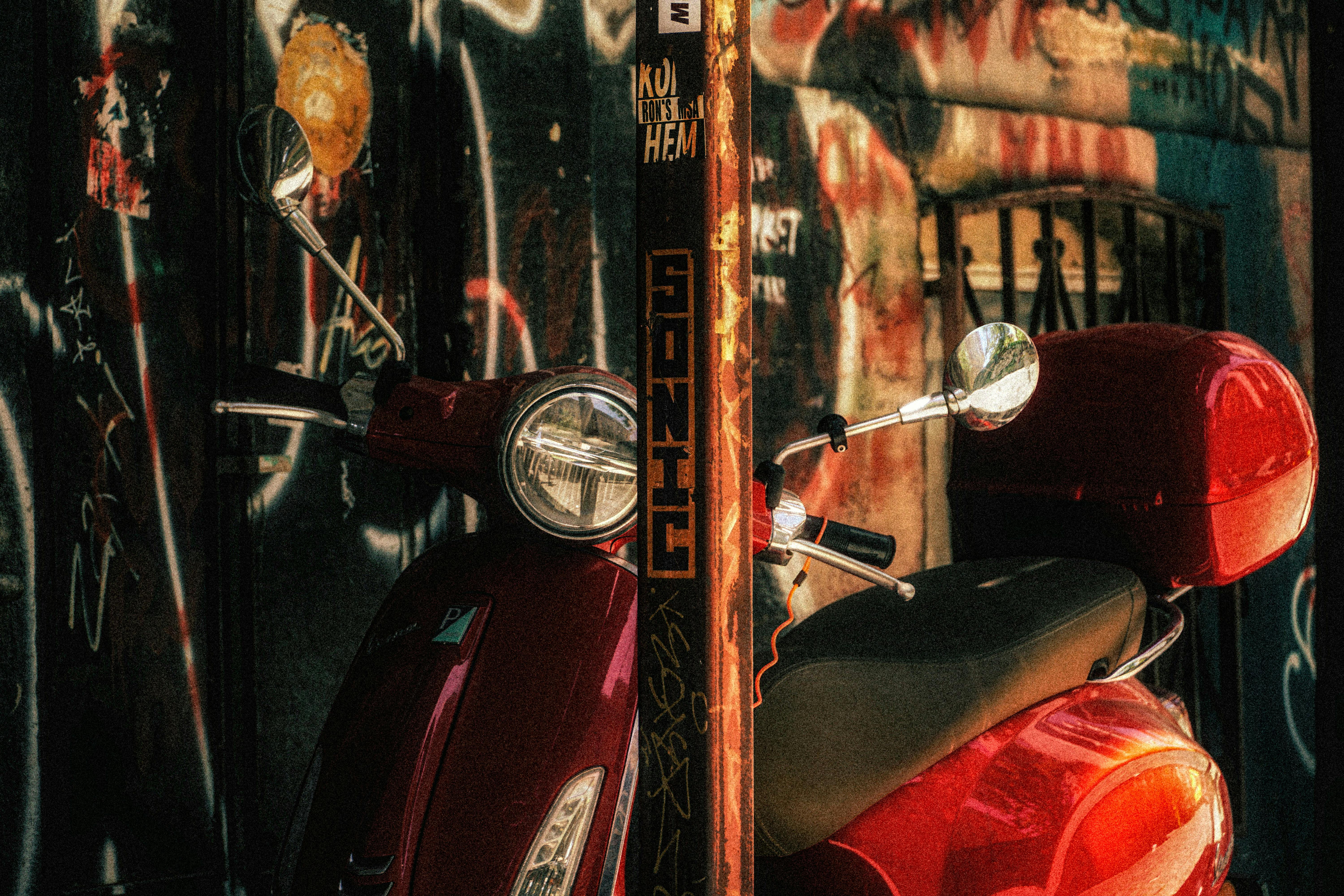 A vintage red scooter parked against an urban graffiti-covered wall, exuding a retro city vibe.