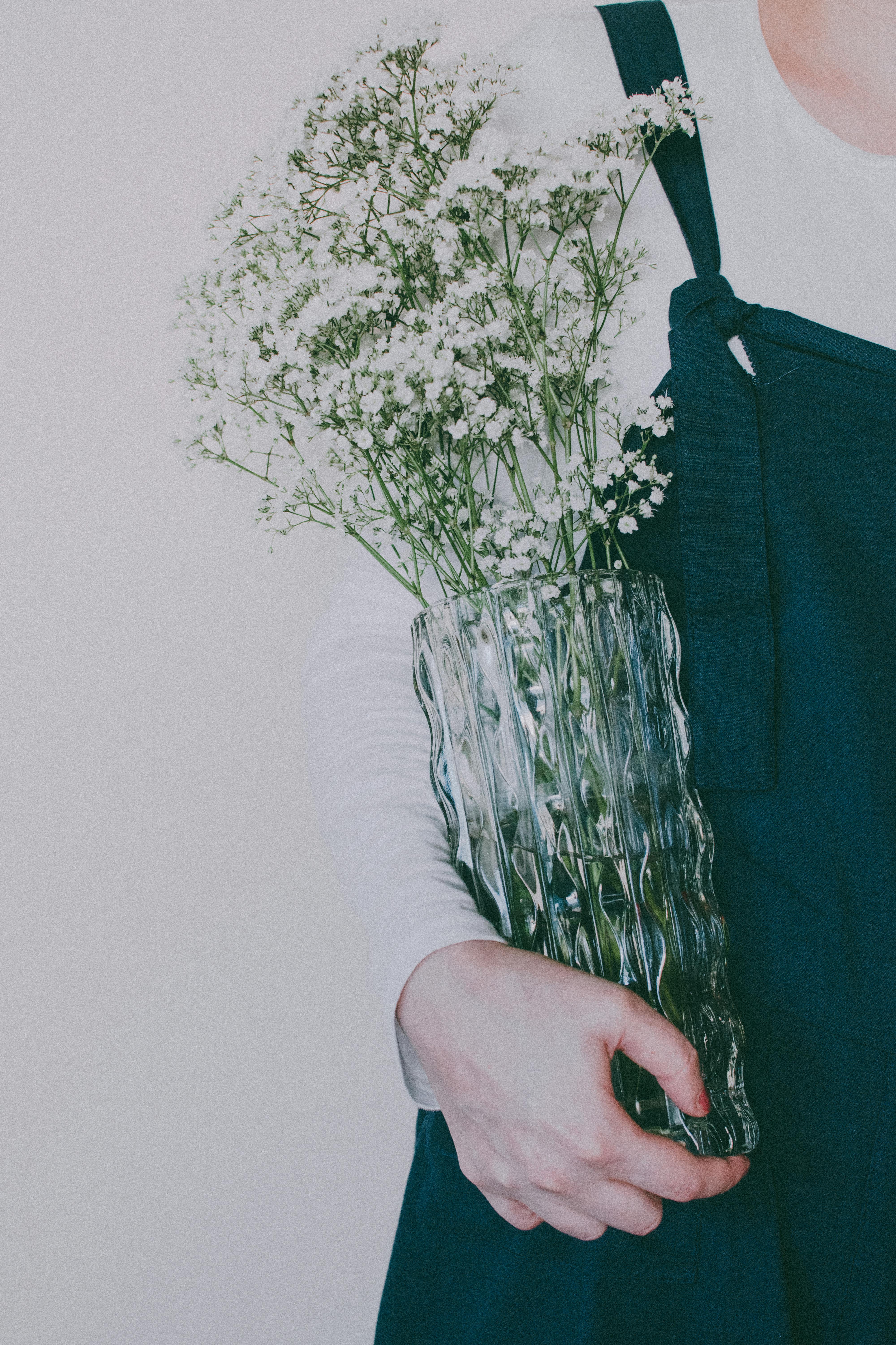 Stylish arrangement of baby's breath in a glass vase, held by a person in casual attire.