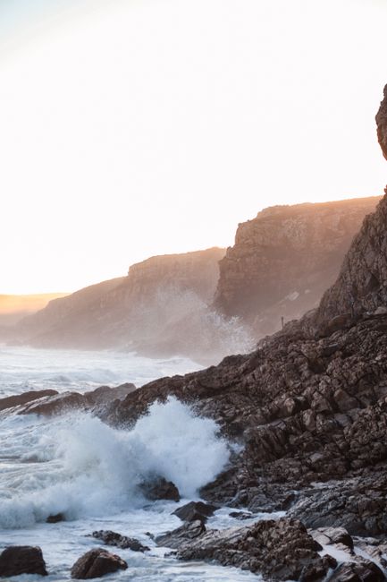 Capture the dramatic waves crashing against rocky cliffs at sunrise along South Africa's stunning coastline.