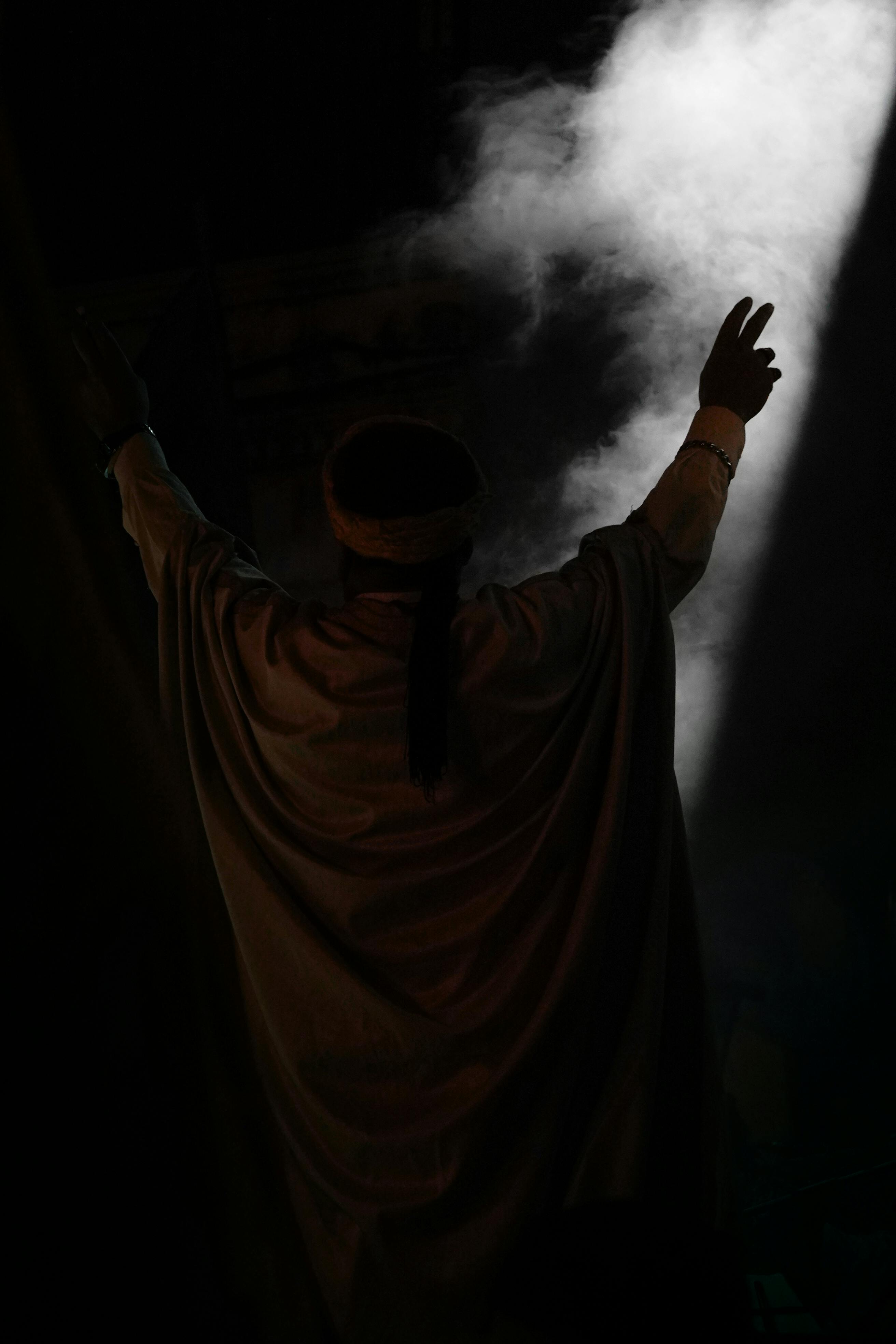 Gratuit Une silhouette lève les bras sous un projecteur dramatique, créant une ambiance mystique. Photos