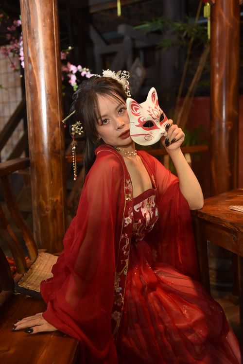 Free A woman in a traditional red dress holds a fox mask, embodying mystery and cultural elegance. Stock Photo