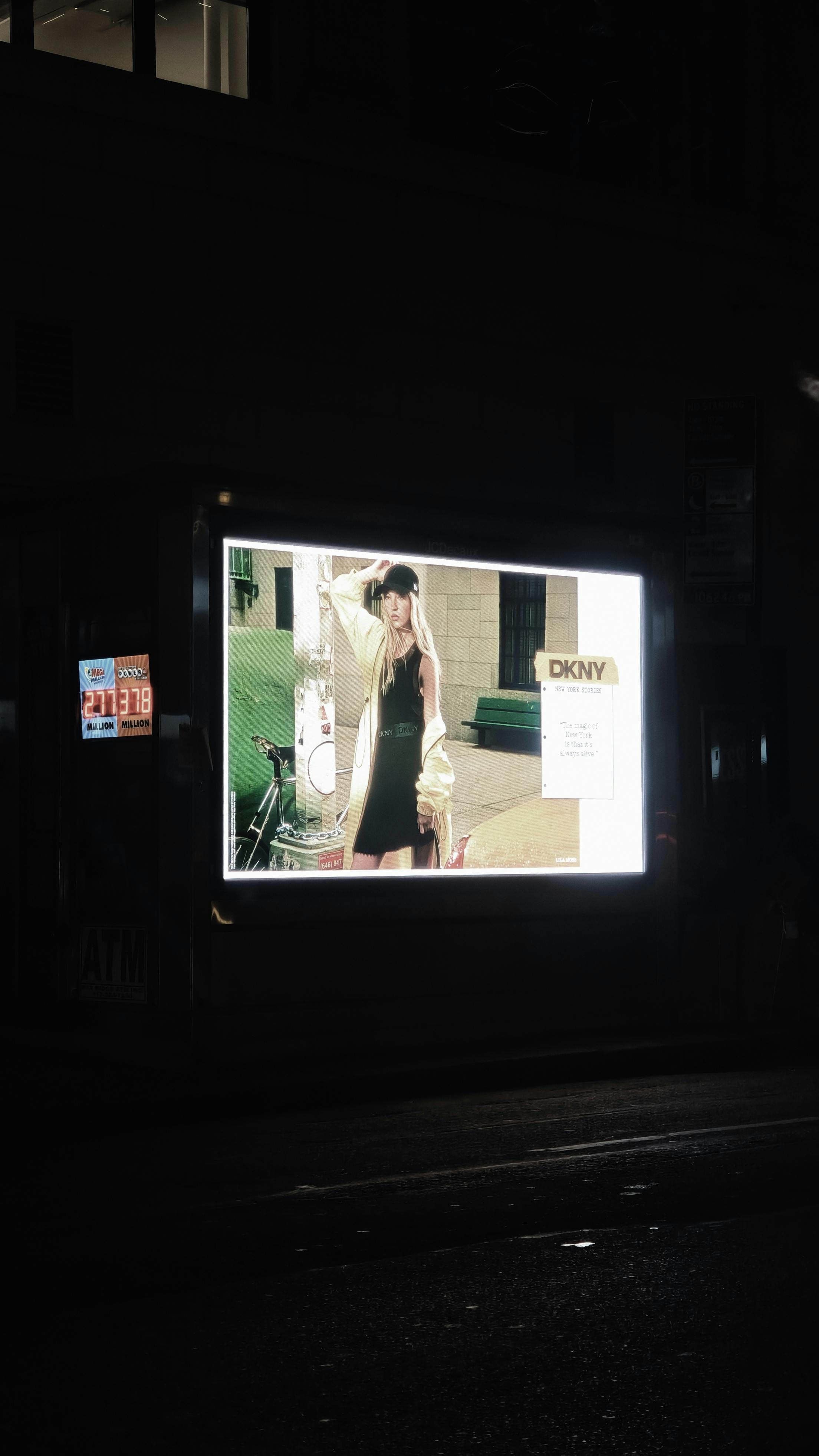 Outdoor illuminated fashion billboard featuring DKNY advertisement at night on a city street.