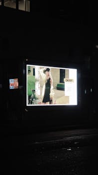Outdoor illuminated fashion billboard featuring DKNY advertisement at night on a city street.