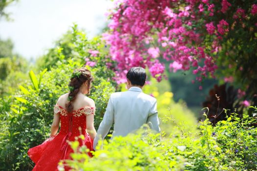 Couple in elegant attire enjoying a walk in a colorful garden.