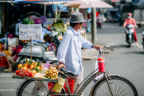 Free Man on bicycle selling fresh fruit in a lively outdoor market setting. Stock Photo