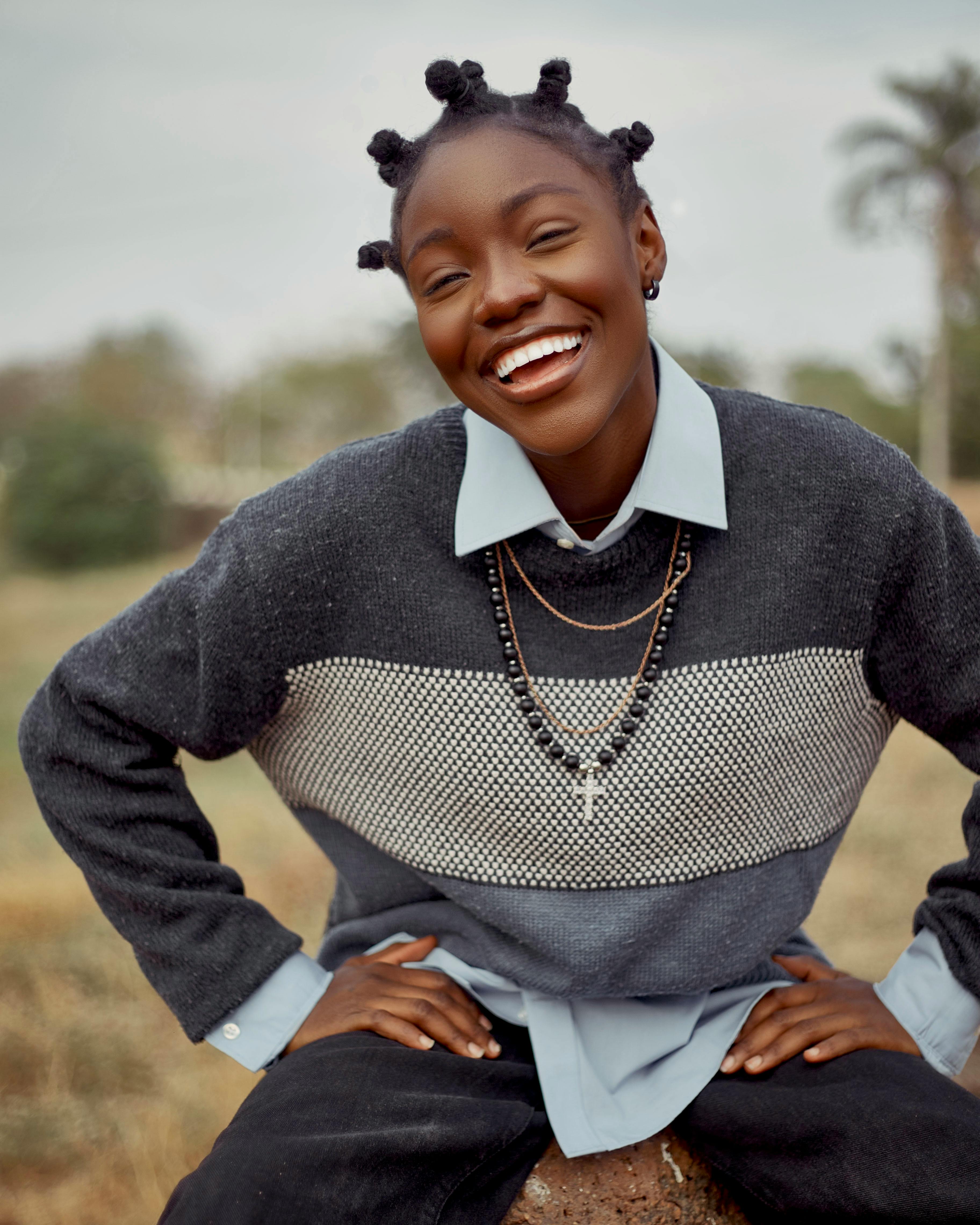 Young woman wearing sweater laughs joyfully in a natural setting.