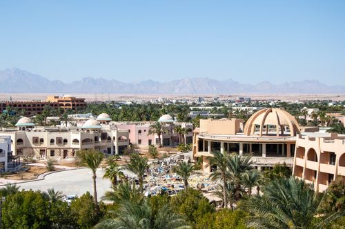 Free Aerial shot of a desert resort town with domed buildings and palm trees against mountain backdrop. Stock Photo
