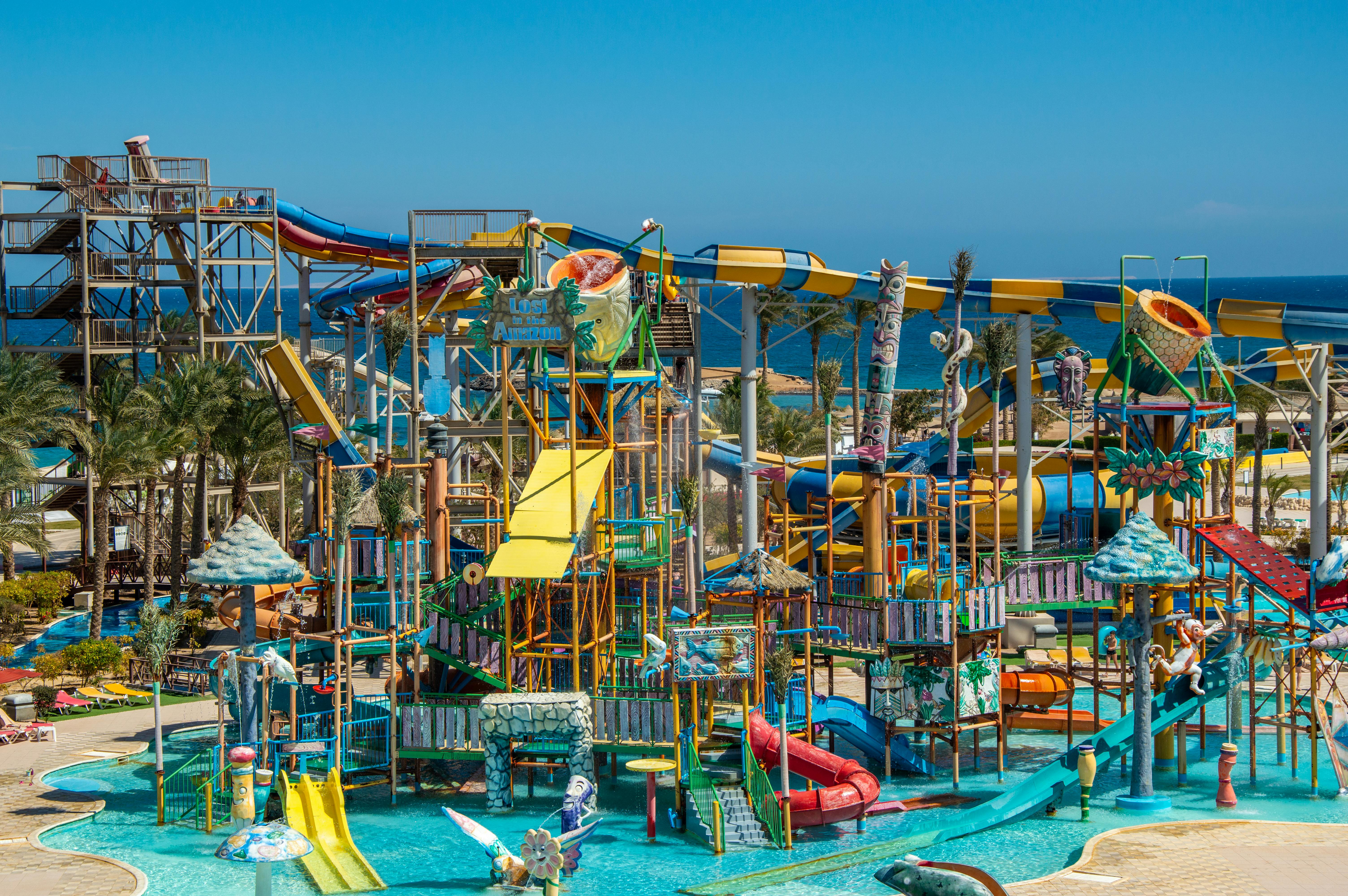 A lively water park with colorful slides, pools, and palm trees by the sea.