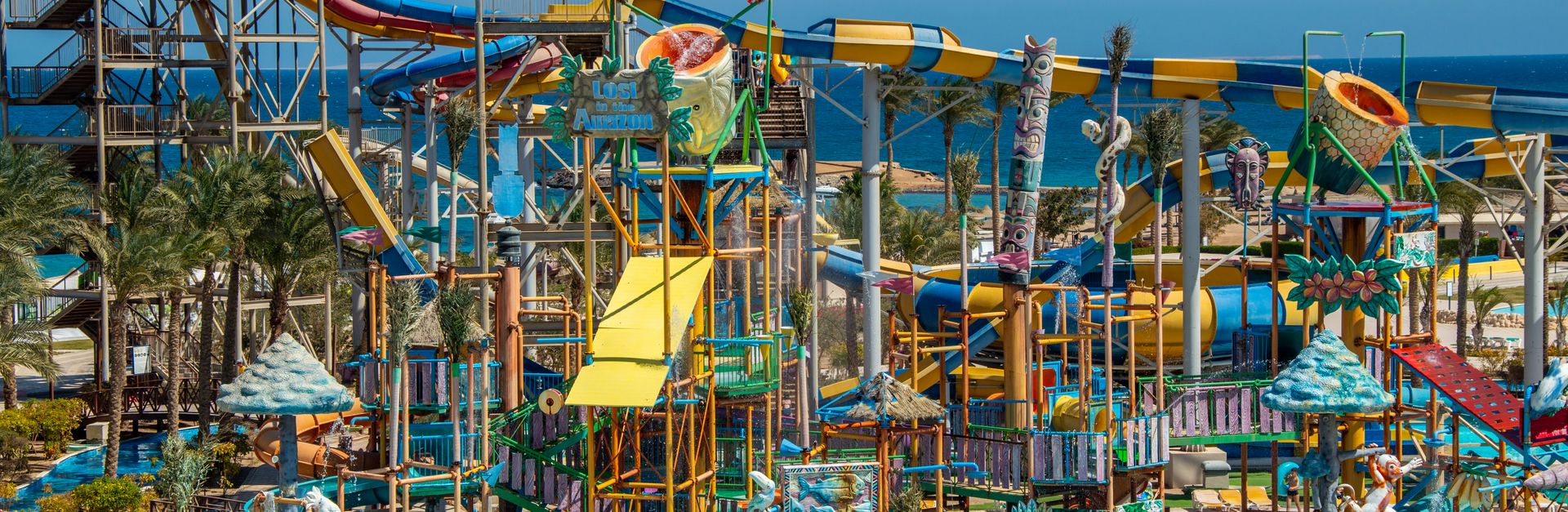 A lively water park with colorful slides, pools, and palm trees by the sea.