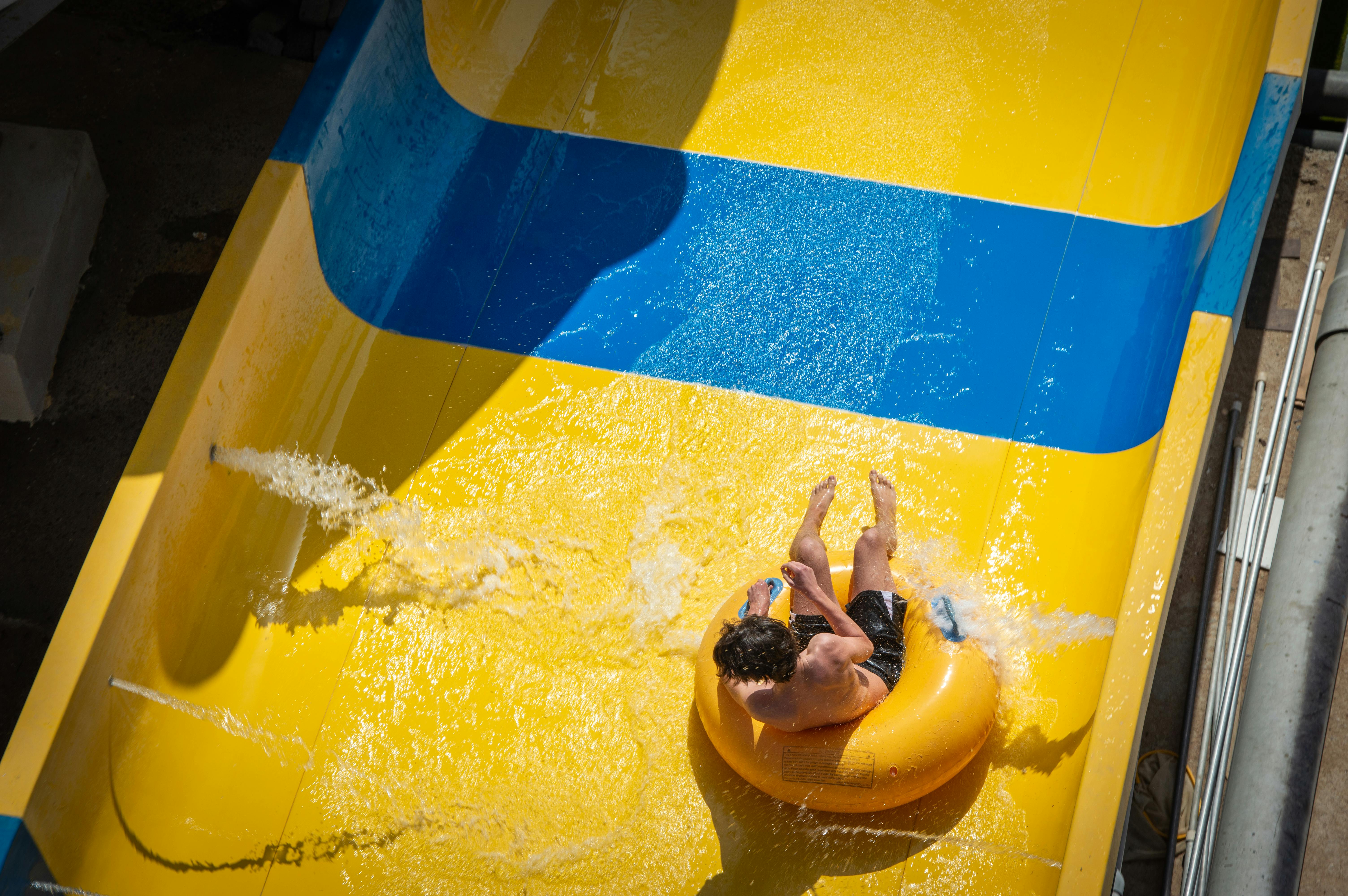Person enjoying a thrilling ride down a colorful yellow and blue water slide in the sunshine.