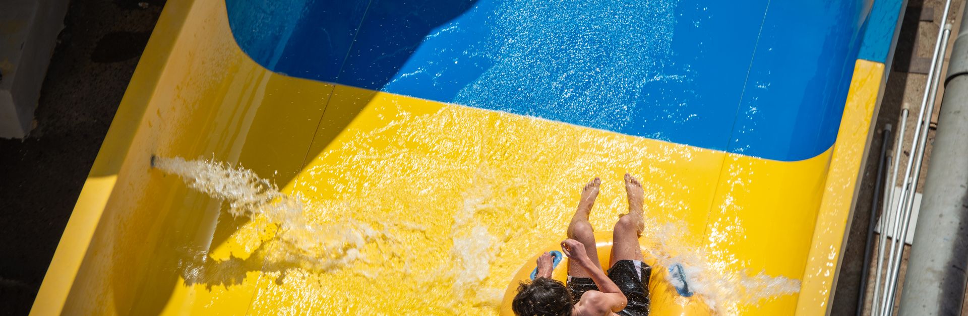 Person enjoying a thrilling ride down a colorful yellow and blue water slide in the sunshine.