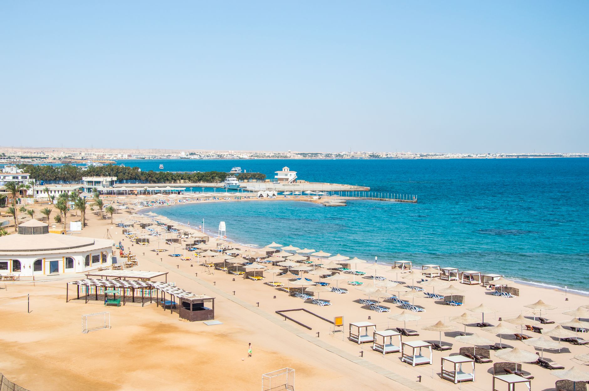 Aerial view of a serene beach resort with umbrellas, calm blue sea, and sandy shore.