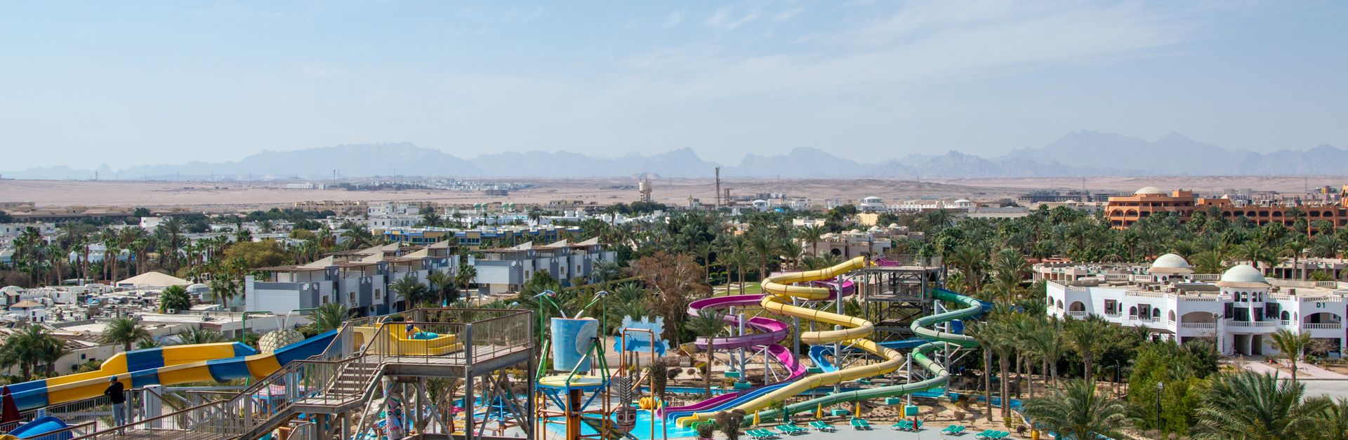 Aerial view of a lively water park with colorful slides and pools on a sunny day, surrounded by dese