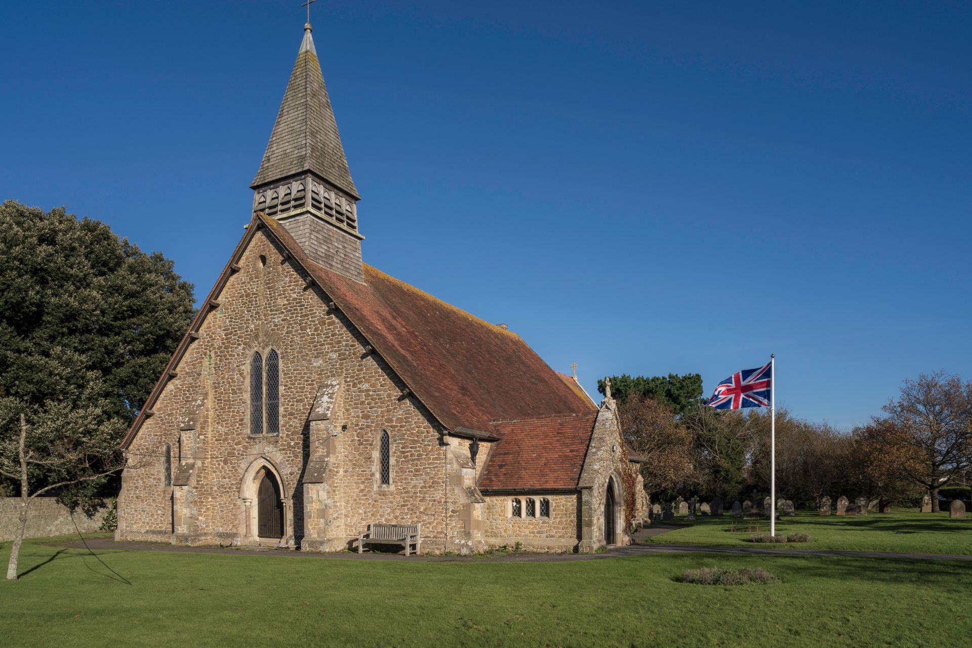 Old stone church with British flag in a peaceful countryside setting.