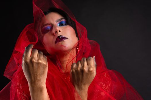 Striking fashion portrait with golden hands and blue makeup in bold red tulle.