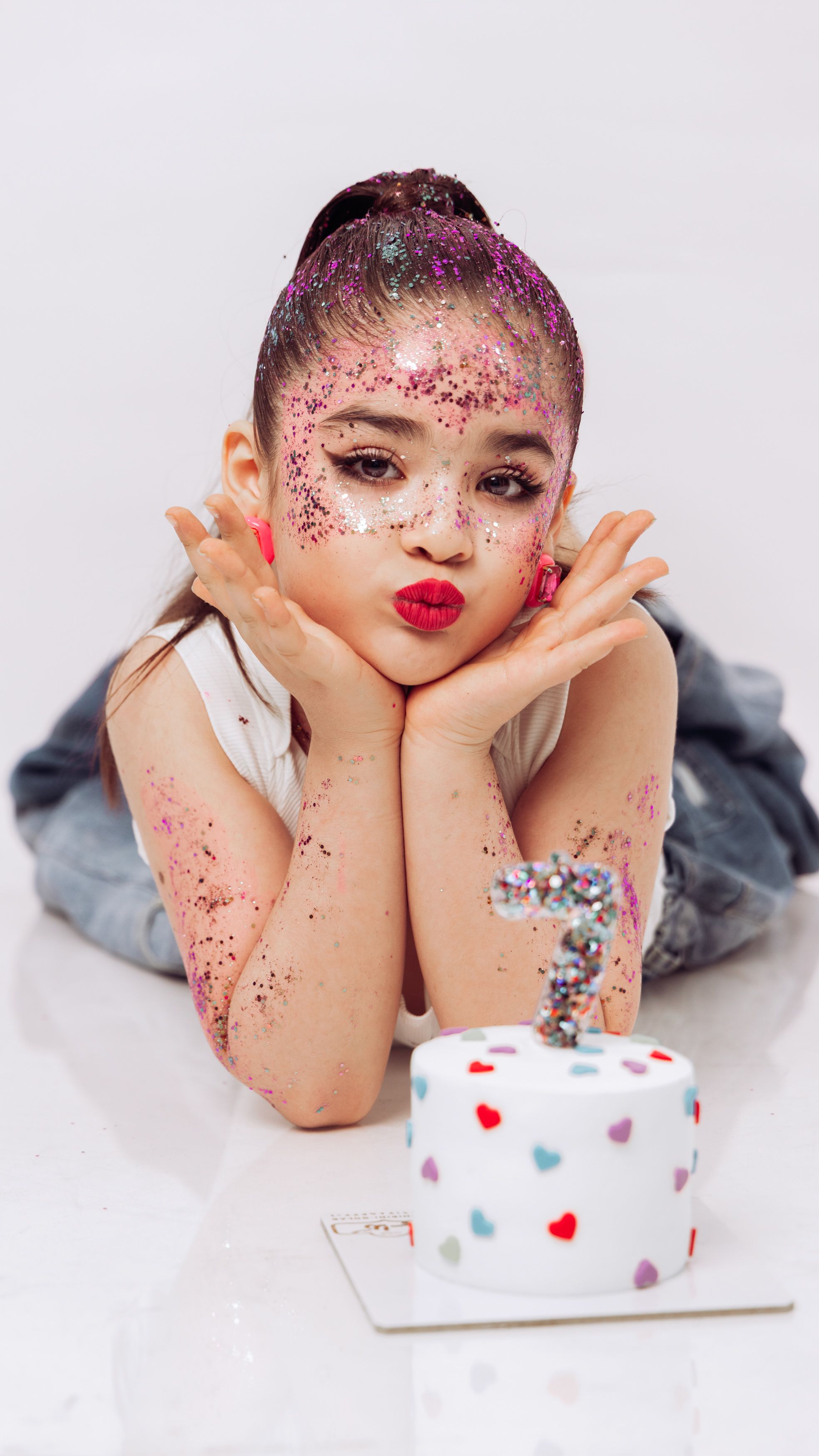 A young girl with glitter makeup celebrates her birthday with a cake.