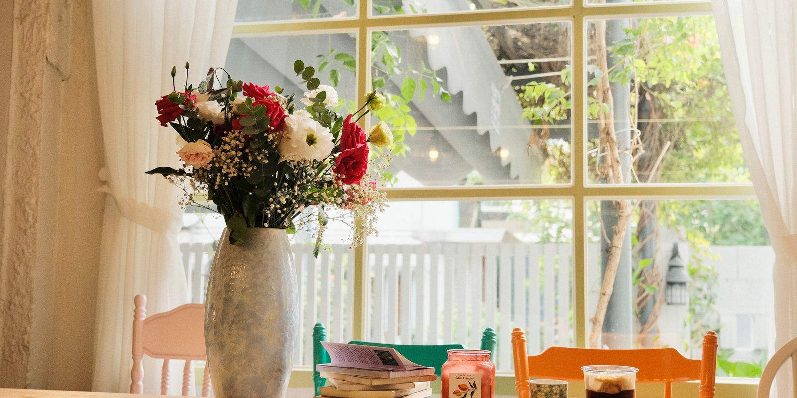 Cozy cafe table with flowers, books, and drinks by a bright window.