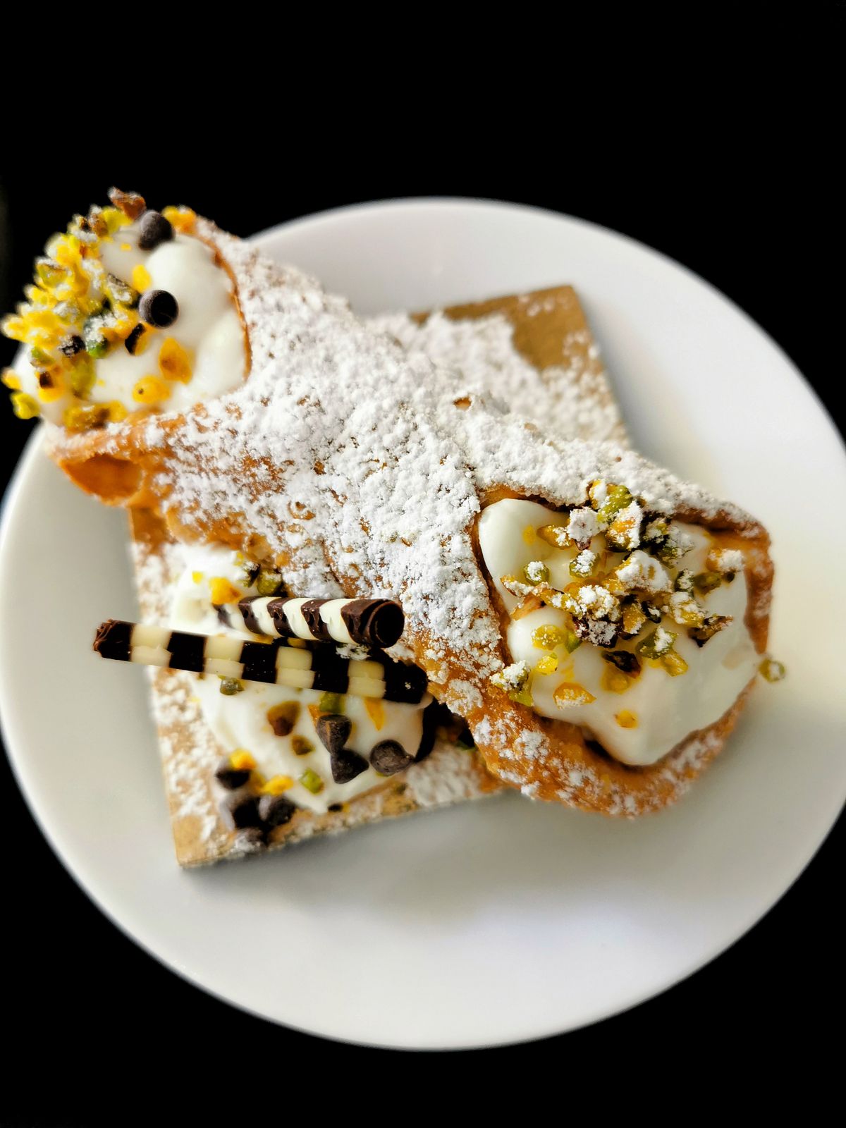 Due cannoli siciliani con ricotta, pistacchio e zucchero a velo