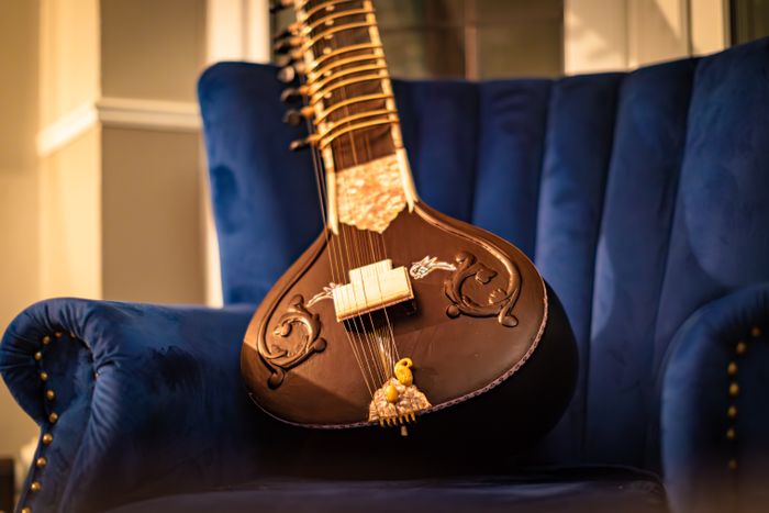 A sitar resting on a blue velvet chair in a quiet room before a performance.