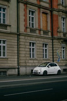 Elegant white Fiat 500 parked on a city street beside a historic building facade.