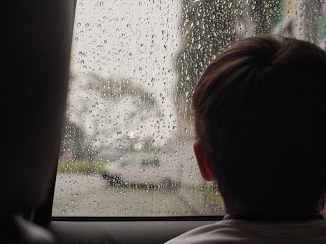 A child looking out a rain-soaked car window, capturing a moment of reflection.
