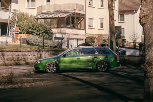 A green luxury car parked outside modern residential buildings on a sunny day, showcasing elegance and urban lifestyle.