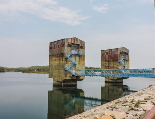 Free Two rusted water control towers stand over a tranquil reservoir with a bridge. Stock Photo