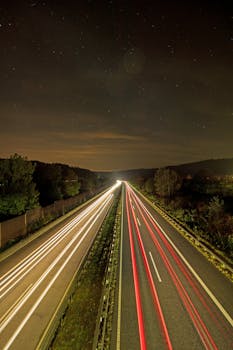 Nighttime highway with light trails under a starry sky, capturing motion and tranquility.