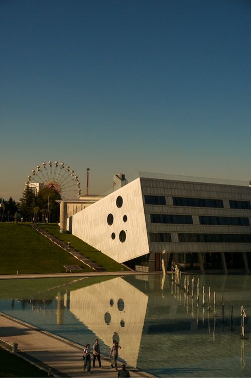 Free View of a modern building and ferris wheel reflected in a pond at sunset. Stock Photo