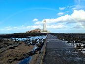 Scenic view of St Mary's Lighthouse on a clear day with a rainbow and blue sky.