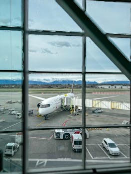 A parked airplane at the airport with a mountain view through a terminal window, showing preparation for boarding.