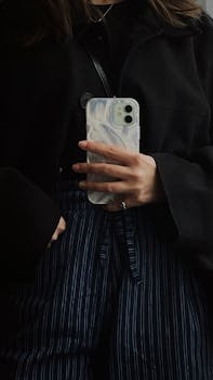 Minimalist reflection photo capturing a stylishly dressed person holding a smartphone with a marble case.