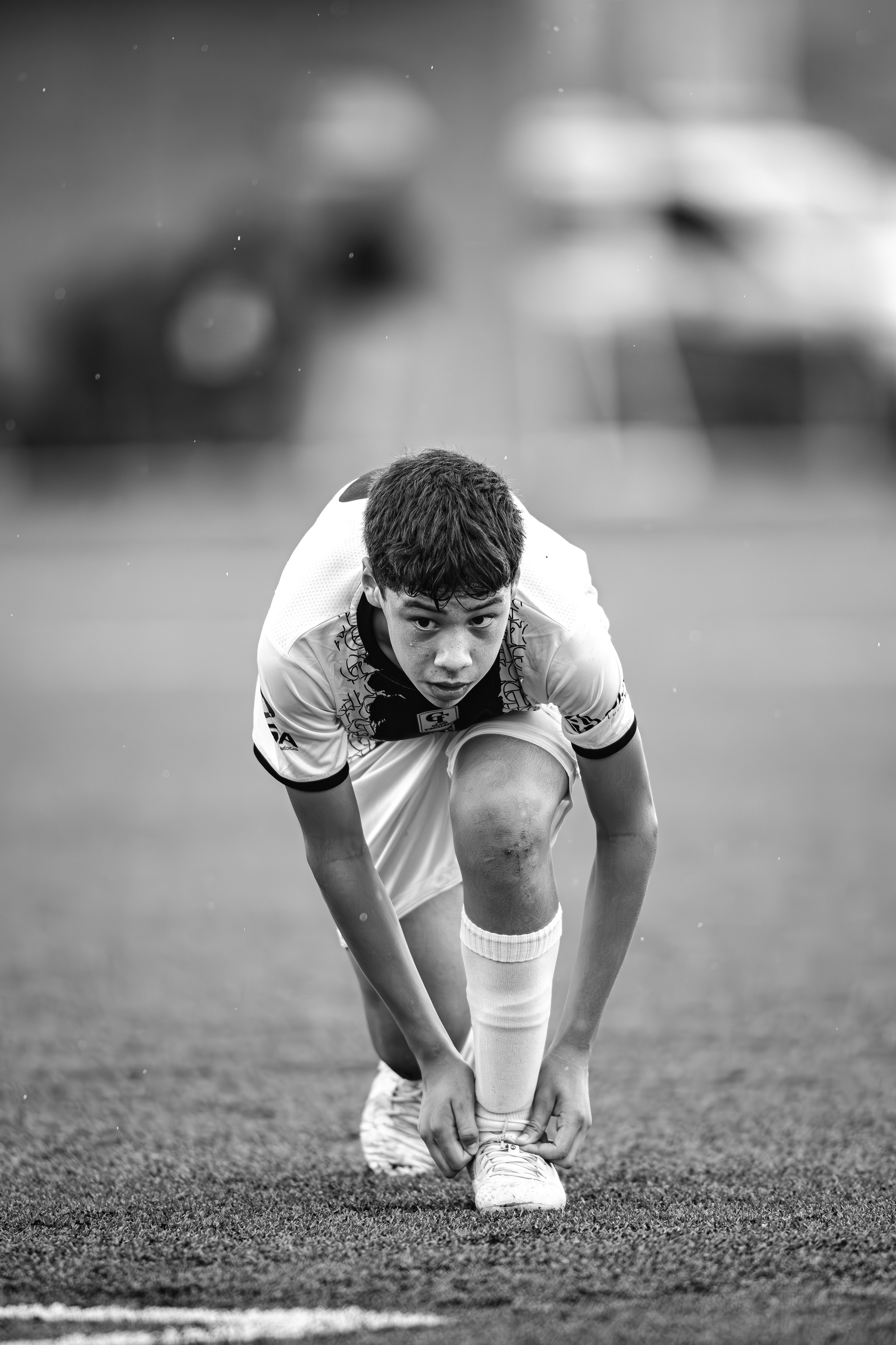 Black and white photo of a teenage soccer player tying shoelaces before a match.