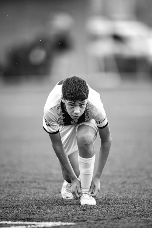 Free Black and white photo of a teenage soccer player tying shoelaces before a match. Stock Photo