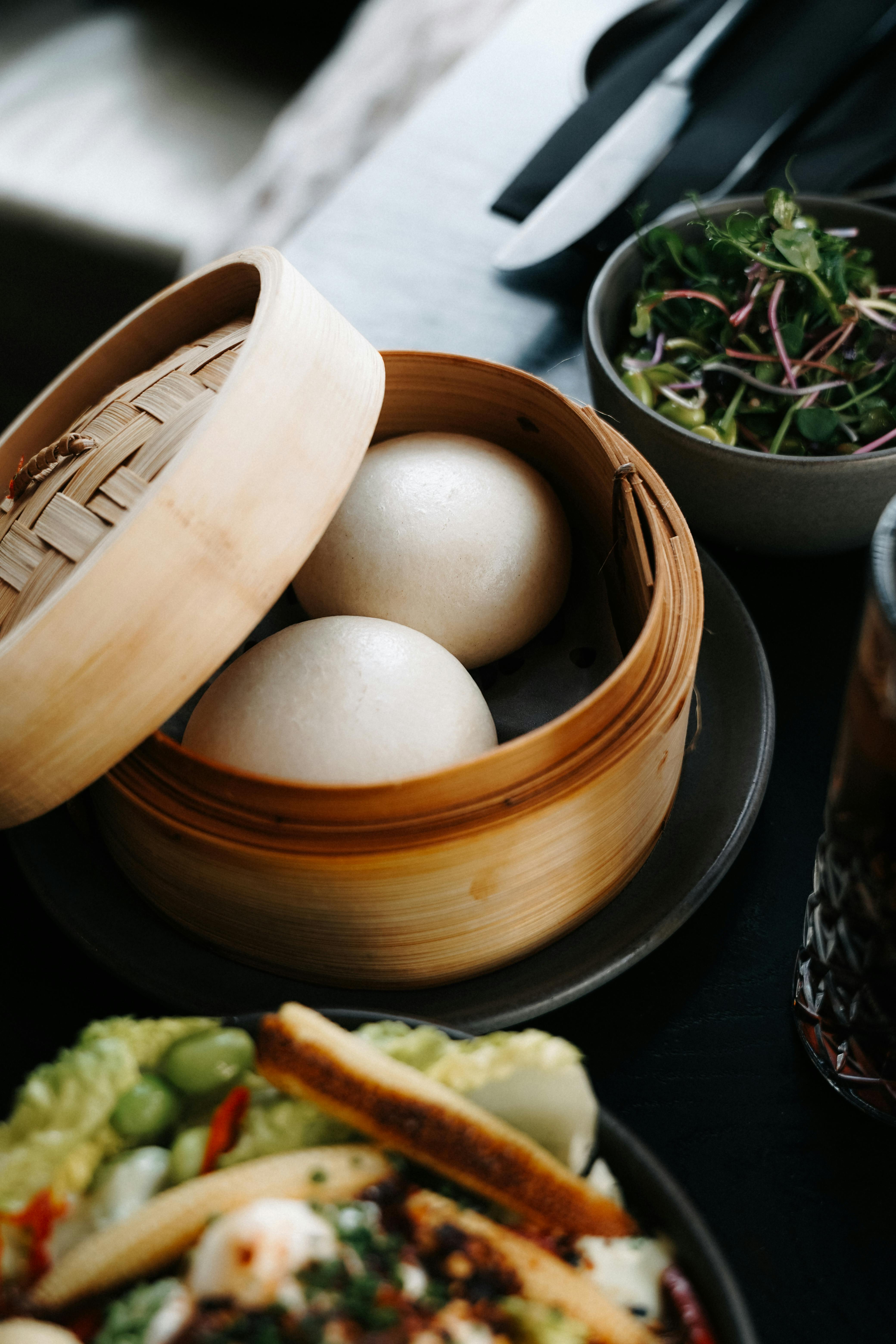 Steamed buns served in a bamboo steamer with salad and greens, ideal for food lovers.