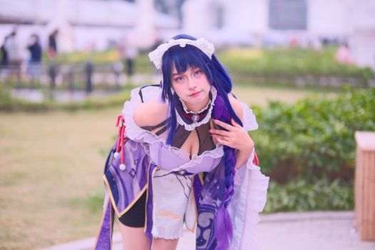 A person in vibrant cosplay costume posing in an outdoor garden area.