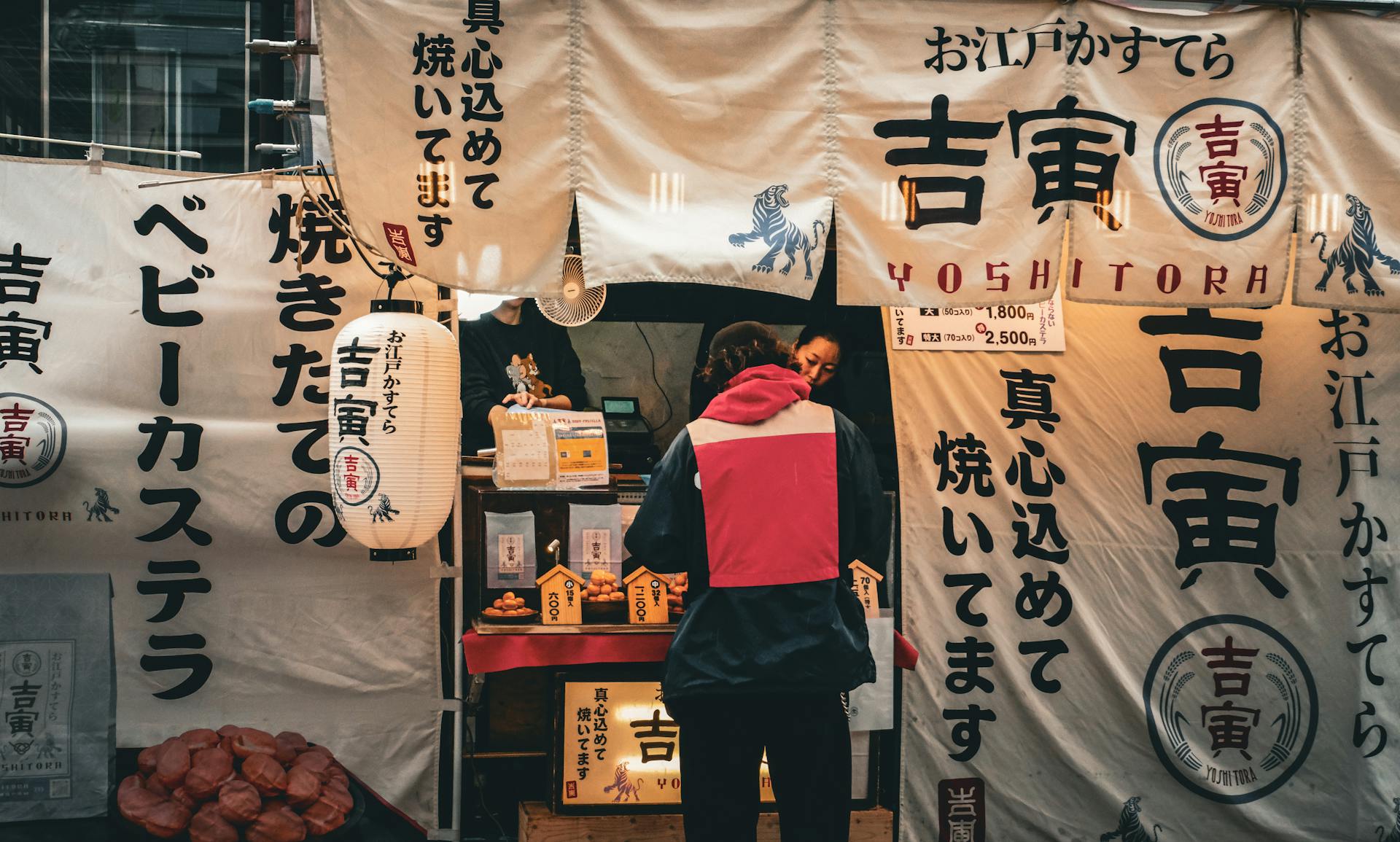 A traditional Japanese street food stall with banners and a customer buying snacks.