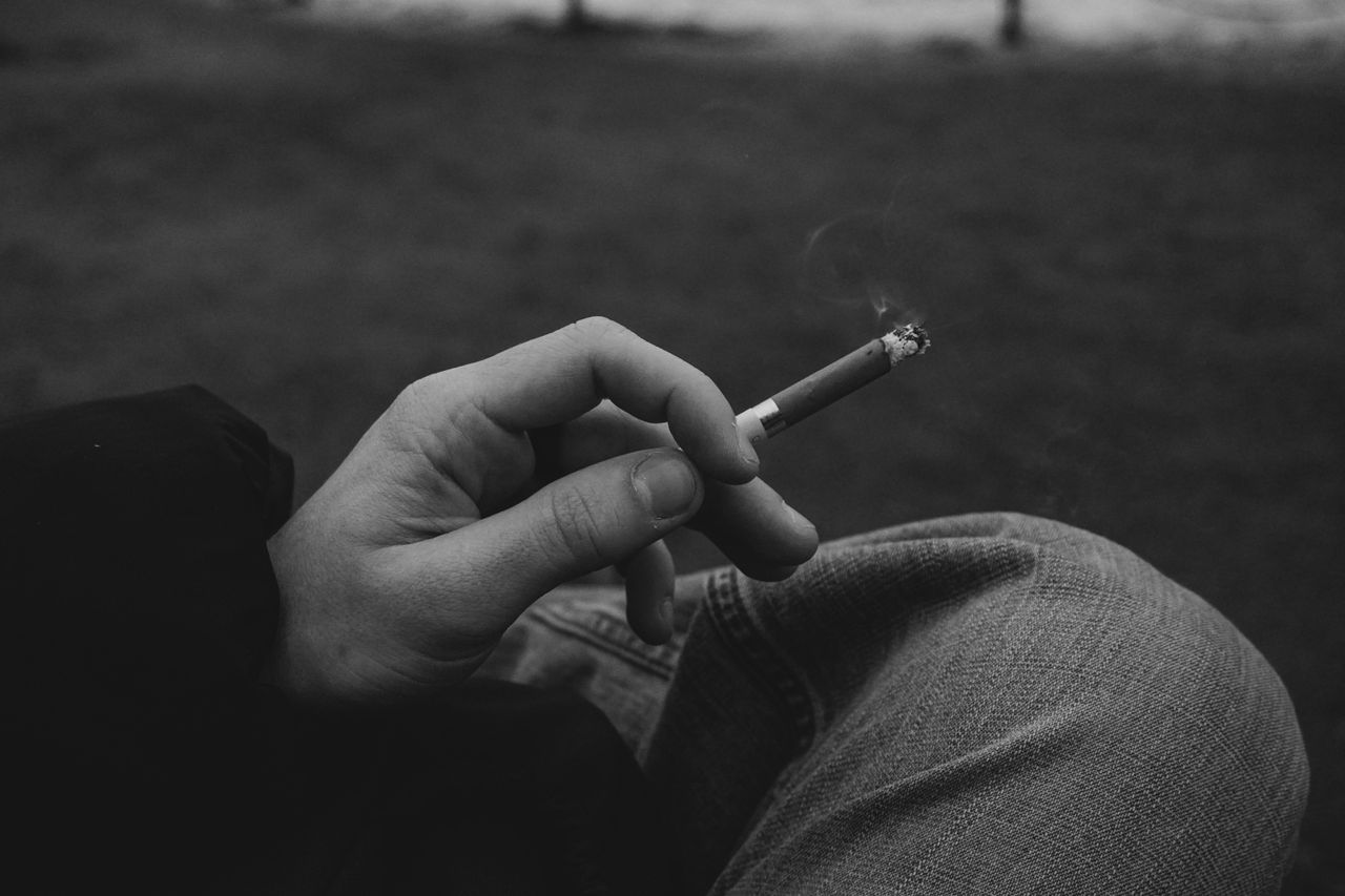 monochrome image of a hand holding a cigarette outdoors smoke rises in